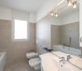 modern bathroom with bathtub, bidet, toilet, sink, mirror, and tiled walls