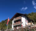 2 story house, white exterior, red shutters, wooden balconies, stone wall, flag