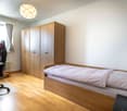 bedroom with bed, desk, chair, radiator, wooden wardrobe, lamp