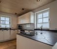 modern kitchen with white cabinets, black countertops, island with induction cooktop, windows, wooden floor