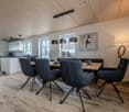 Dining room with wooden floor, wooden dining table, modern chairs, pendant lights, white cabinets, kitchen area, windows, artwork, lamp