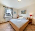Bedroom with bed, nightstands, lamps, window with curtains, radiator, picture frames, tiled floor, wardrobe