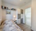 single bed, nightstand with lamp, white wardrobe, picture frame, shelves with books, radiator
