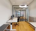 modern office room with white walls, wooden floor, glass walls, desks, chairs, monitors, cabinets