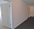 Empty hallway with white walls, wooden floor, gray carpet, and windows