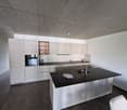 modern kitchen with white cabinets, black countertops, stainless steel island, built-in oven, sink with faucet, glasses on countertop
