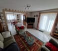 white tiled floor, large windows, white curtains, couch, armchair, coffee tables, TV, entertainment center, dining table, chairs, wooden cabinet, shelves, decorative items
