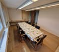 Empty room with a long table, chairs, windows, and a radiator