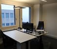Two desks, two chairs, computer monitor, lamp, trash bin, water bottles, building view