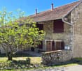 Stone house, brown roof, wooden doors, windows with shutters, small garden, tree in front