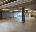 Empty room with concrete floor, brick walls, multiple windows, central pillar, and fire extinguisher