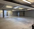 Empty warehouse room, concrete floor, brick wall, exposed beams, ceiling lights, emergency lights