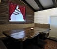 Wooden walls, window with red curtains, large wooden table, bench seating, central heating radiator