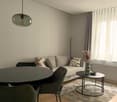 A round table and chairs, a white sofa with decorative pillows, a round metal side table, a floor lamp, a vase, a round glass pendant light.