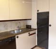 The image shows a kitchen with white cabinets, a stainless steel sink, a dishwasher, and a black refrigerator. The countertop appears to be made of a light-colored material, possibly granite or laminate. The walls are painted a light color, and the ceilin