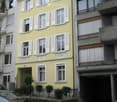 3-story yellow building with white shutters, balconies, and a garage on the ground floor