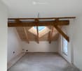 empty room with wooden trusses, skylight window, and unfinished floor