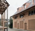 Wooden exterior, raised ground floor, slanted roof, windows, multiple doors, wooden deck with stairs