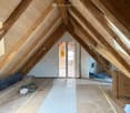 Unfinished attic room with wooden beams, windows, and unfinished floor