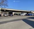 A large commercial building with multiple garage bays and a parking lot in front. The building has a metal exterior and appears to be used for automotive services or repairs, with several cars parked in the lot.