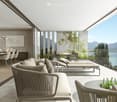 Spacious open-plan living area with large windows offering a scenic view of the lake and mountains. The room features modern, minimalist furniture including a sectional sofa, dining table and chairs. The outdoor terrace with lounge chairs provides additio