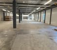 Warehouse, large open space, steel beams, concrete floor, metal ceiling, white walls, no furniture, empty, boxes in corner