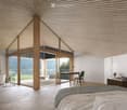Spacious bedroom with high vaulted ceiling, large windows offering a scenic mountain view, wooden beams, and a desk area with a chair