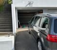 House exterior, white walls, concrete steps, car parked outside garage, metal handrails, open garage with storage items inside
