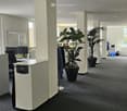 empty office room with carpeted floor, white walls, windows, pillars, coat rack, computer desk, computer monitors, plants
