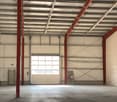 large open warehouse with a wide door, concrete floor, steel columns, metal sheeting, windows on one side