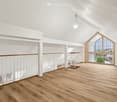 a large attic space with hardwood floors, white walls, two arched windows, a wooden railing, and staircase
