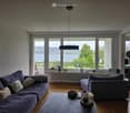living room with a lake view, wooden floor, couch, armchair, coffee table, large windows with balcony access