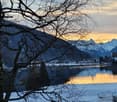 Snowy landscape with a lake, mountains, and a small house