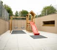 outdoor play area with swing, slide, and small tiles for safety