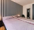 bedroom with a double bed, bedside tables, striped wall, open walk-in shower, wooden floor