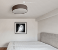 white bed, gray headboard, picture frame with black and white photo, white ceiling lamp, wooden floor