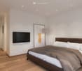 White walls, wooden floor, king-size bed, flat screen TV, floor lamp, bedside stool