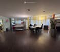 empty room with wooden floor, white walls, desks, chairs, monitor, potted plants, lamps, storage