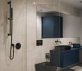 a bathroom with a shower, sink, and toilet with a glass shower enclosure, blue cabinet, and mirror