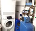 A stacked washing machine and dryer next to a water softener and blue barrels
