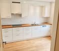 kitchen with white tiles, wooden counter, stainless steel sink, dishwasher, white cabinets, wooden floors
