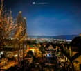 Cityscape with illuminated houses, buildings, and cityscape at night, visible mountains in the distance.