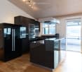 modern kitchen with sleek black cabinetry, marble countertops, modern appliances, island, stainless steel fridge, oven, microwave, extractor fan, balcony, glass sliding doors, hardwood floors, views of the surrounding area