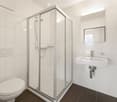 glass shower stall, white tiled walls, white porcelain sink, modern faucet, white toilet, mirror, tiled floor