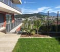 Private outdoor area with garden, fence, plants, balcony with railings, clear blue sky, mountain view