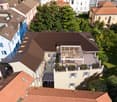3 story beige building with brown roof, balconies, and large terrace with pergola