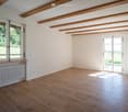 empty room, white walls, wooden ceiling, wooden floors, two windows, one with balcony, white radiator