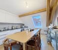 open kitchen, wooden dining table, chairs, white cabinets, wooden beams, kettle, coffee machine, sink, faucet, window