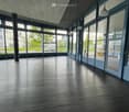 Empty large room, grey tiles, wooden floor, windows, pillars, large entrance doors
