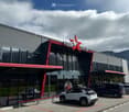 A large modern building with a red star logo and 'VIDA LOCA' text above the entrance, large glass windows, and cars parked in front.
